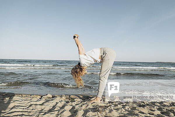 Woman with blond hair practicing stretching exercise on beach