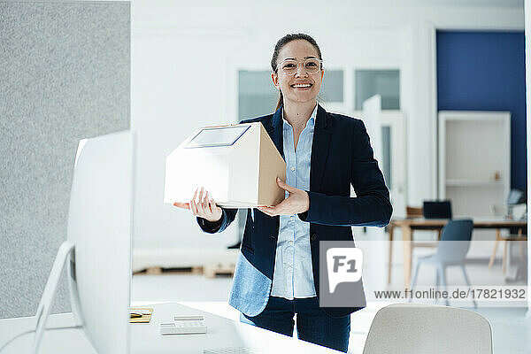 Happy businesswoman with solar panel on model house in office
