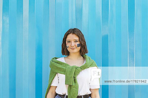 Smiling teenage girl with peace symbol and European Union paint on cheeks standing in front of blue cargo container
