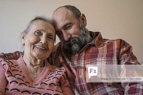 Smiling senior woman with mature man sitting in front of wall