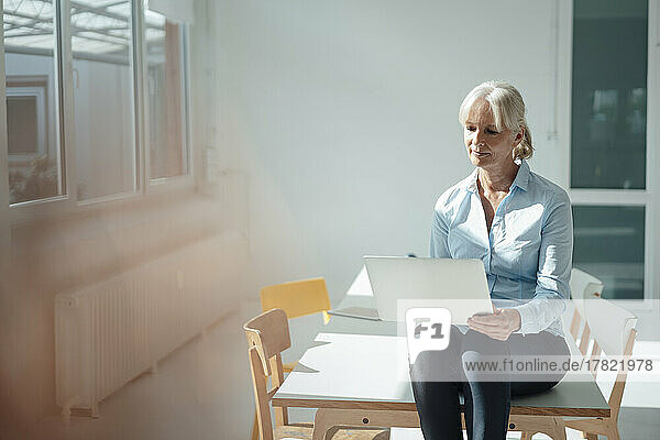 Senior businesswoman using laptop sitting on desk in office