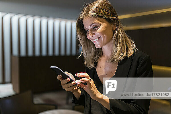 Happy businesswoman using smart phone in lobby at hotel