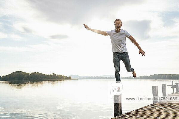 Happy mature man balancing on wooden post of pier
