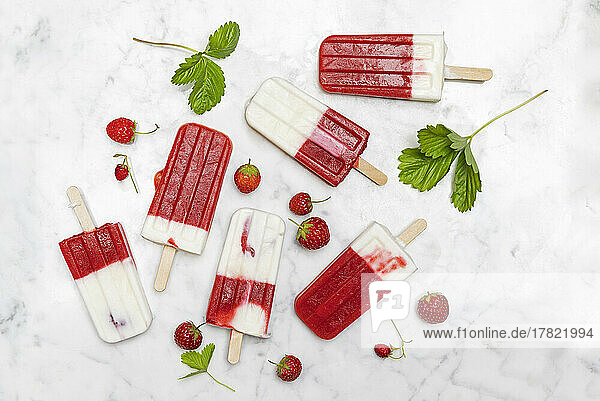 Homemade strawberry-yogurt popsicles flat laid against white marble
