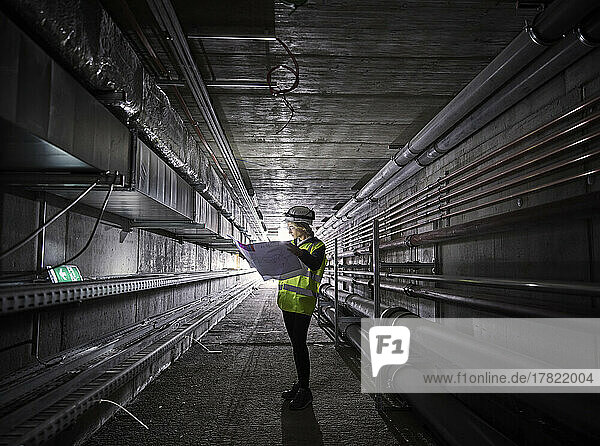 Young engineer looking at blueprint standing in tunnel