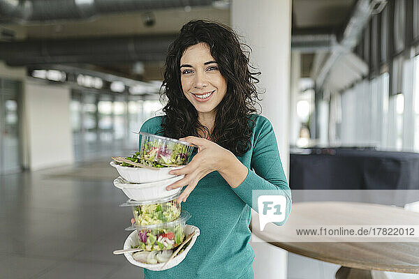 Happy businesswoman holding stack of salad in office