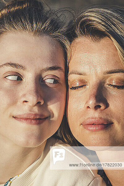 Smiling teenage girl looking at mother with eyes closed