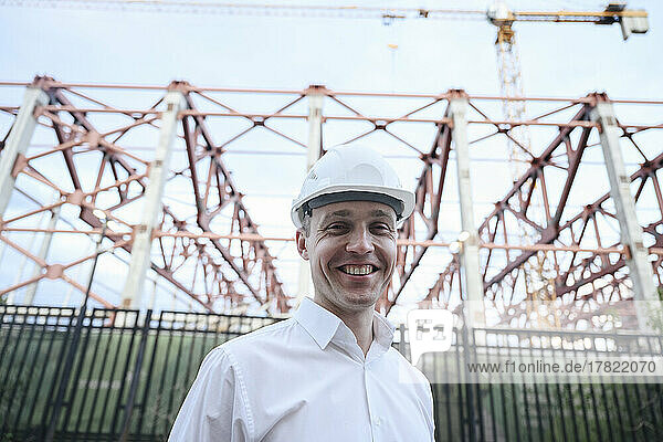 Happy engineer wearing hardhat standing in front of construction frame