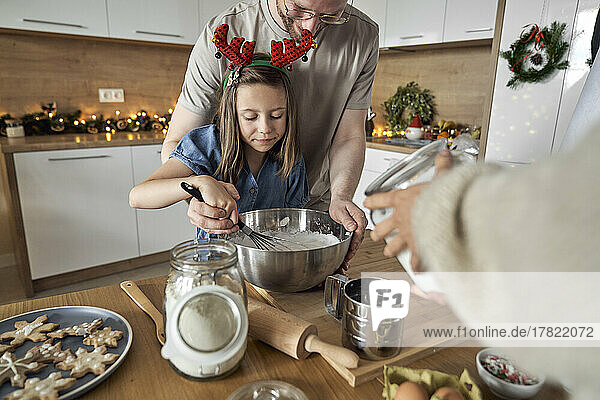 Lächelnder Mann mit Tochter  die in der Küche Keksteig mischt