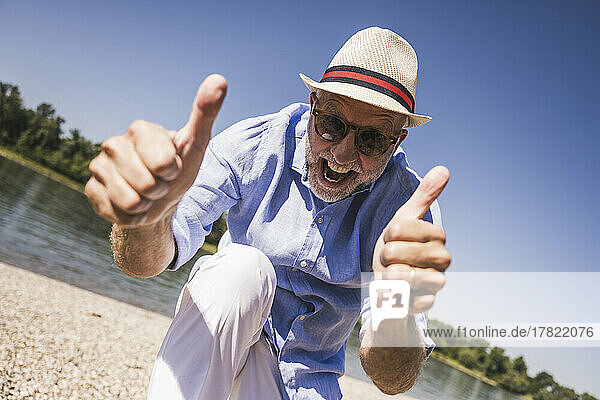 Happy senior man gesturing thumbs up at riverbank