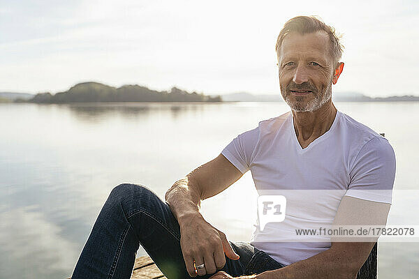 Smiling mature man sitting near lake on sunny day
