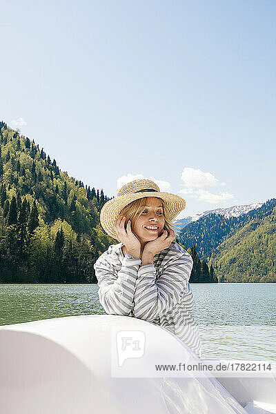 Lächelnde Frau mit Hut genießt an einem sonnigen Tag eine Bootsfahrt im Ritsa-See
