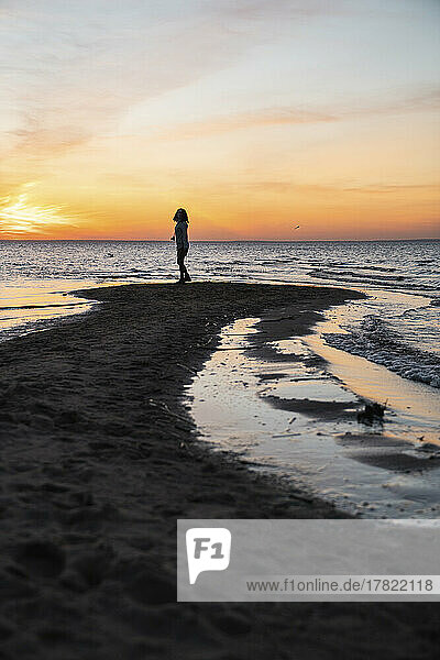 Junge Frau steht bei Sonnenuntergang an der Küste