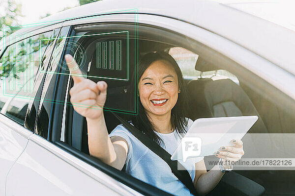 Glückliche reife Frau  die im Auto sitzt und einen Tablet-PC auf einem virtuellen Bildschirm verwendet