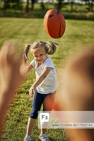 Smiling girl throwing rugby ball to brother on sunny day