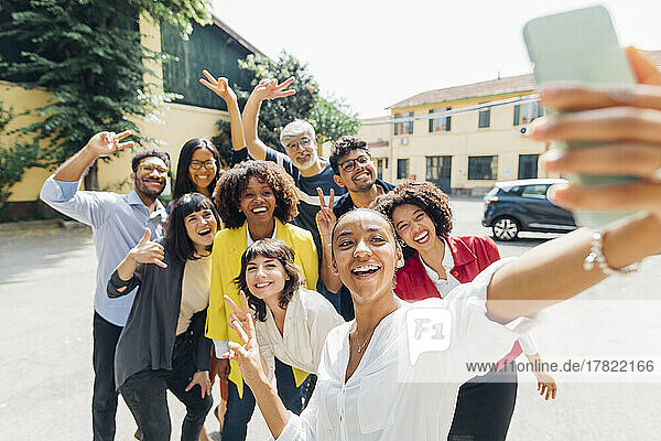 Zufriedene Geschäftskollegen gestikulieren und machen Selfies auf dem Smartphone