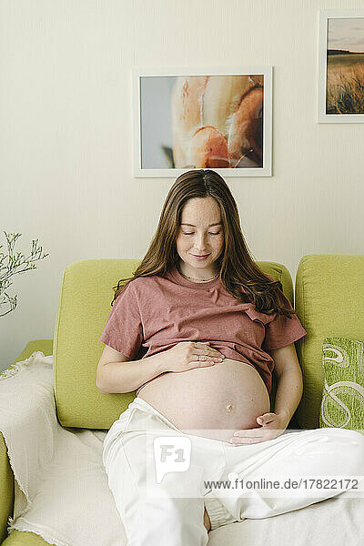Pregnant woman touching abdomen sitting on sofa at home