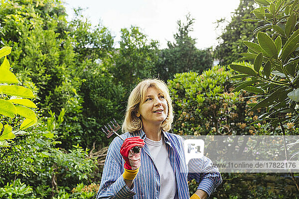Woman holding hand rake standing in garden