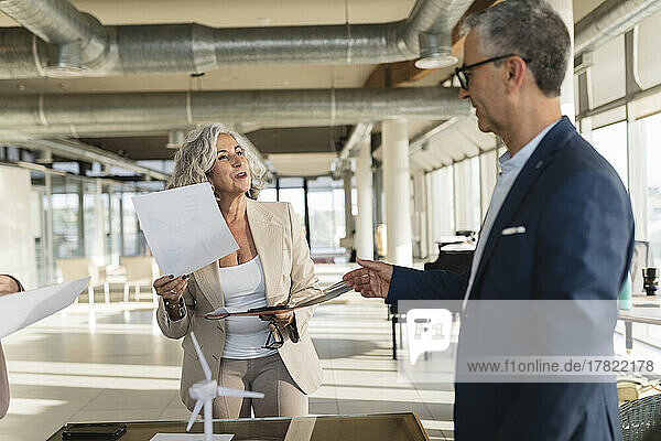 Senior businesswoman holding document talking with colleague at office