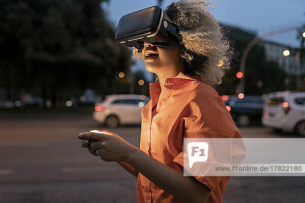 Woman holding controller wearing virtual reality headset at street