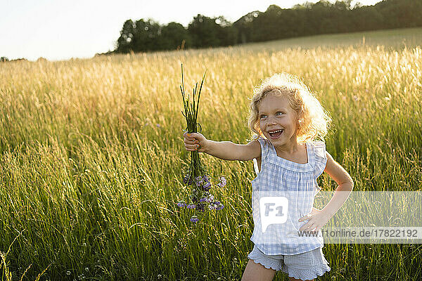 Happy girl standing with hand on hip holding bunch of flower at field