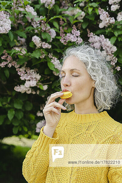 Beautiful woman eating macaroon by tree at park