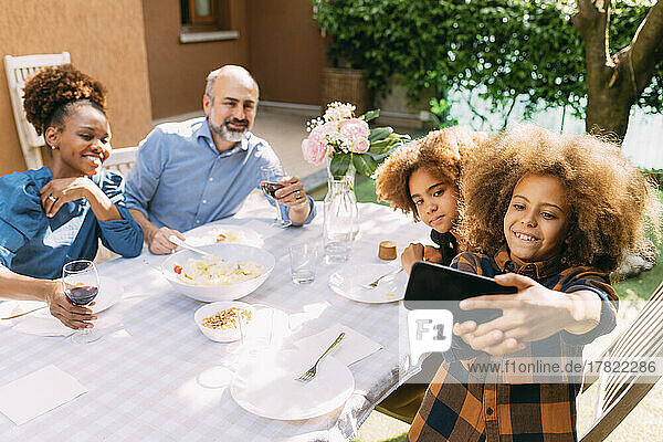 Smiling boy taking selfie with family through smart phone at dining table in backyard