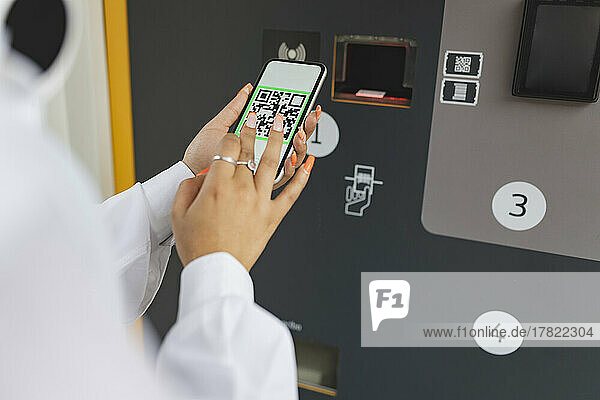 Frau scannt QR-Code über Smartphone in der Nähe von Fahrkartenautomaten