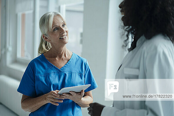 Smiling nurse holding tablet PC talking with female doctor