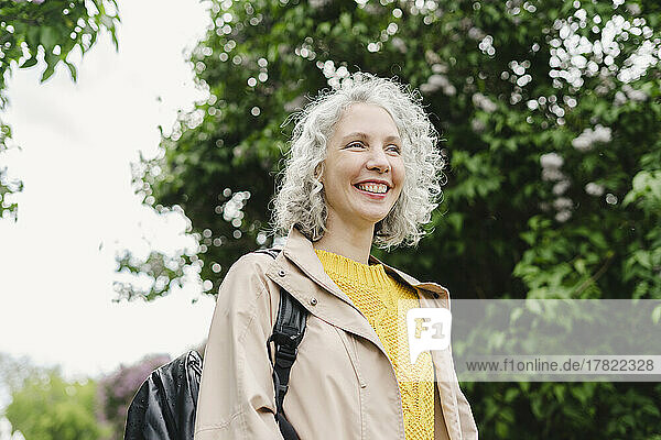Smiling woman with backpack standing in park