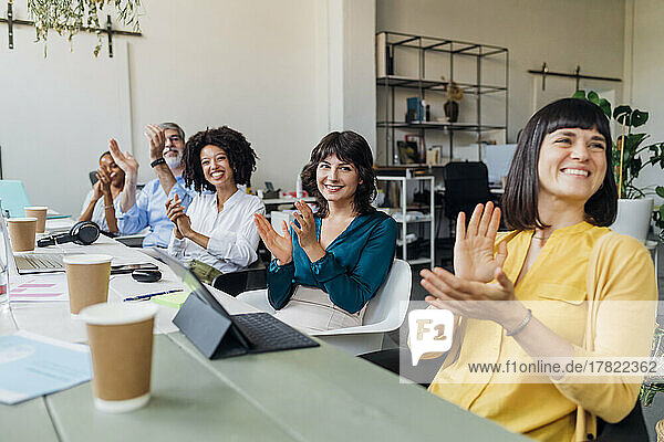 Lächelnde Geschäftsleute und Geschäftsfrauen  die am Schreibtisch im Büro in die Hände klatschen