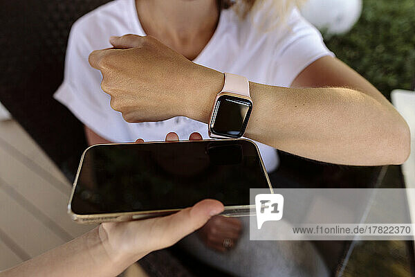 Frau tätigt kontaktloses Bezahlen mit einer Smartwatch auf dem Mobiltelefon  das von der Kassiererin gehalten wird