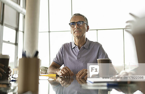 Reifer Geschäftsmann mit Brille sitzt am Schreibtisch