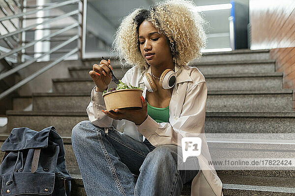 Young woman eating salad sitting on steps