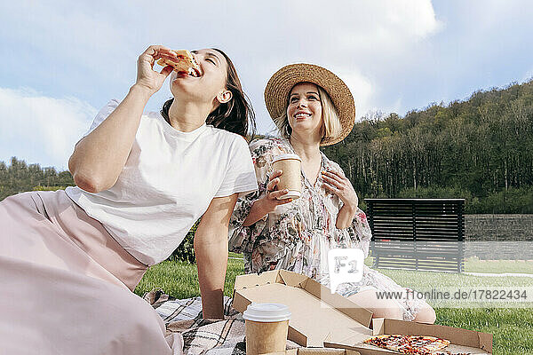 Woman eating pizza by friend in park on weekend
