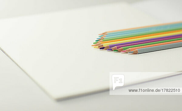 Studioaufnahme einer Reihe von Buntstiften  die auf einem Zeichenpapierblock liegen