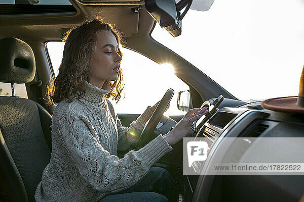 Beautiful young woman using smart phone sitting in car