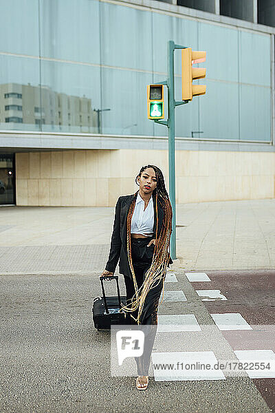 Junge Geschäftsfrau mit Koffer überquert die Straße