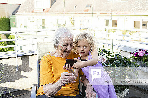 Granddaughter showing mobile phone to grandmother in balcony