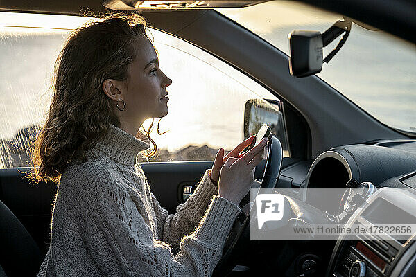 Smiling young woman with smart phone sitting in car