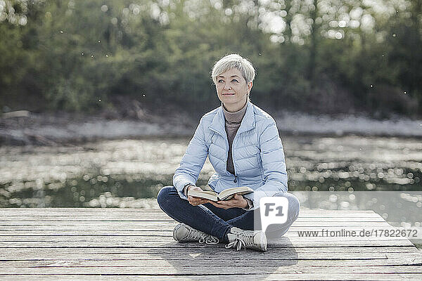 Mature woman sitting cross-legged with book on pier