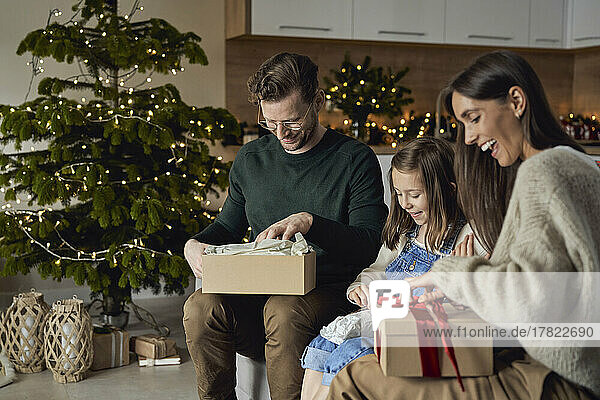Glückliche Eltern mit Tochter öffnen Weihnachtsgeschenk im Wohnzimmer