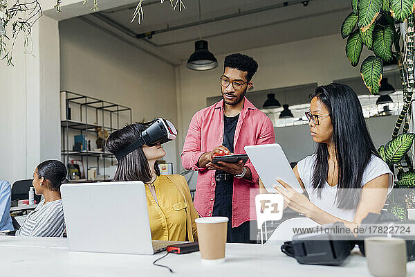 Geschäftskollegen halten Tablet-PCs in der Hand einer Geschäftsfrau mit VR-Brille im Büro