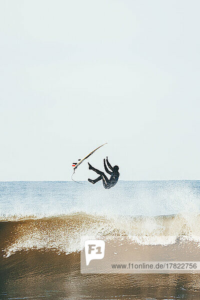 Mann mit Surfbrett springt an sonnigem Tag über das Meer
