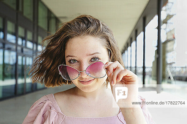 Smiling teenage girl with brown hair wearing pink eyeglasses