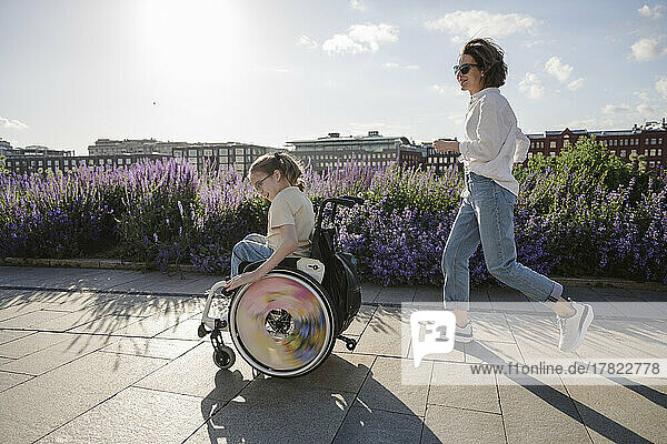Mutter rennt ihrer behinderten Tochter im Rollstuhl im Park hinterher