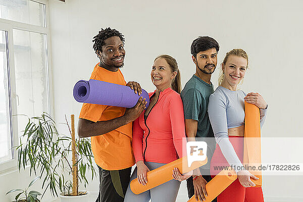 Happy multiracial friends holding exercise mats in yoga studio