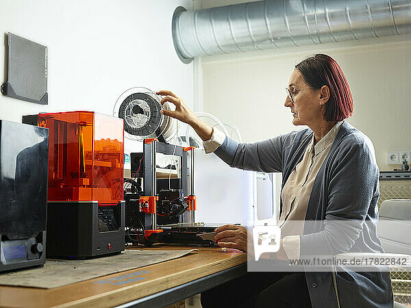 Engineer adjusting filament of 3d printer at workshop