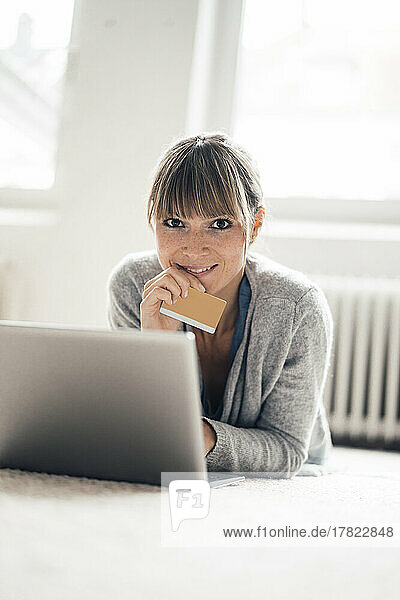 Smiling woman with credit card using laptop at home