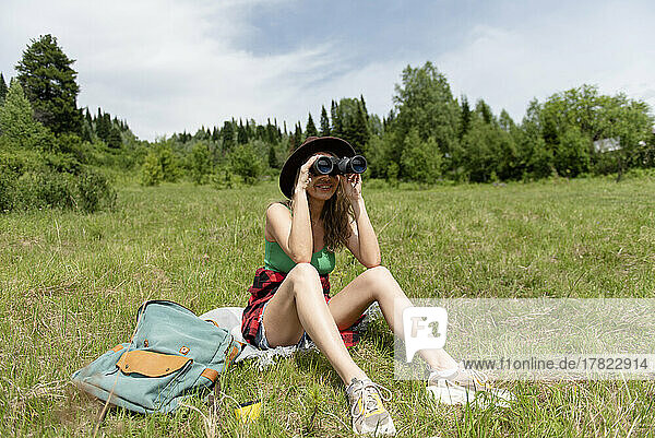 Smiling woman sitting on grass looking through binoculars